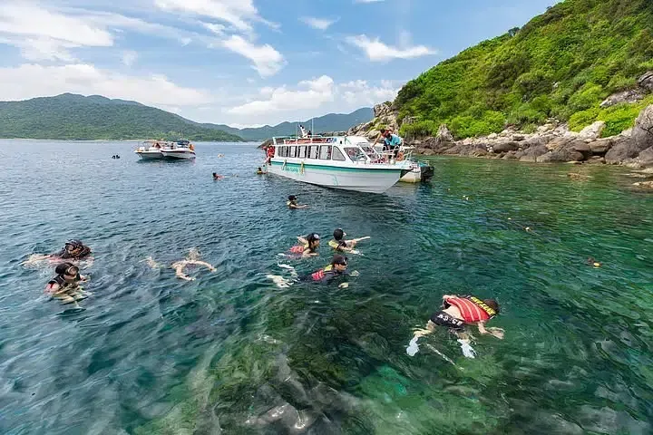Tourists snorkeling in turquoise water near rocky shore during Cham Island boat tour