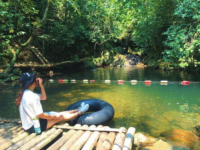 Woman Sitting on a Wooden Platform by Vang Anh Lake, Surrounded by Lush Greenery.
