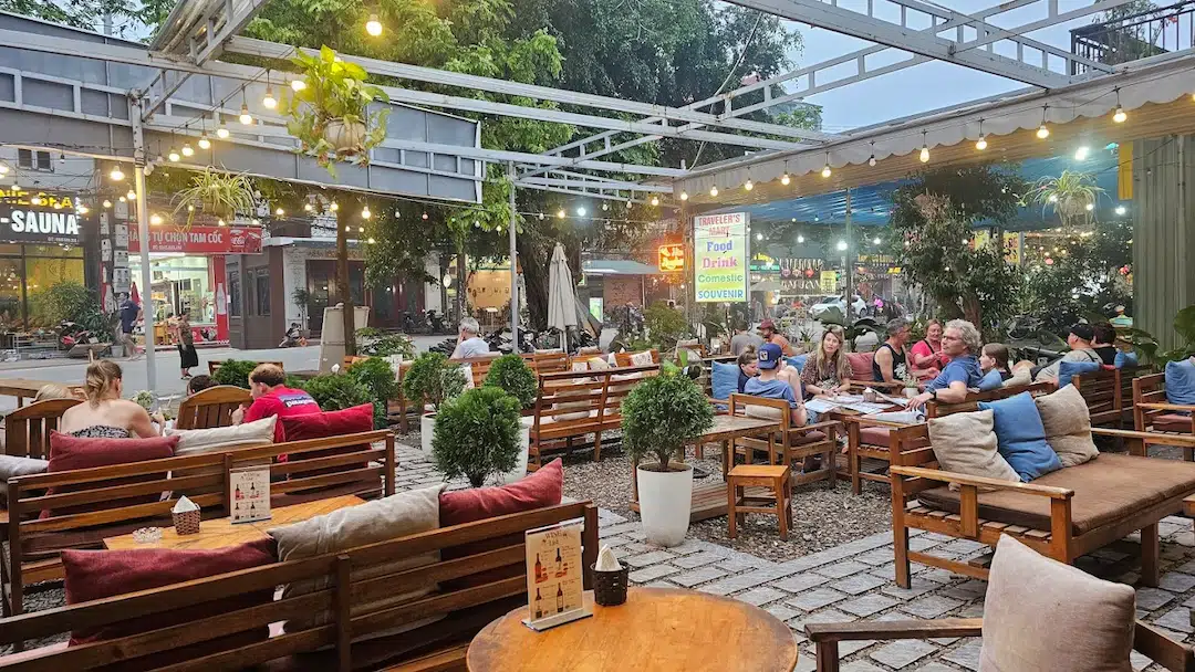 מרפסת מסעדה עם שולחנות עץ ושרשרות אורות בנין בין