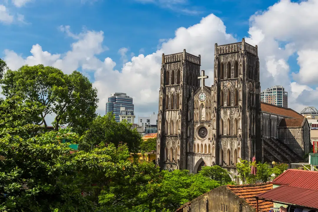 Gothic revival architecture of St Joseph's Cathedral rising above green trees and rooftops in central Hanoi