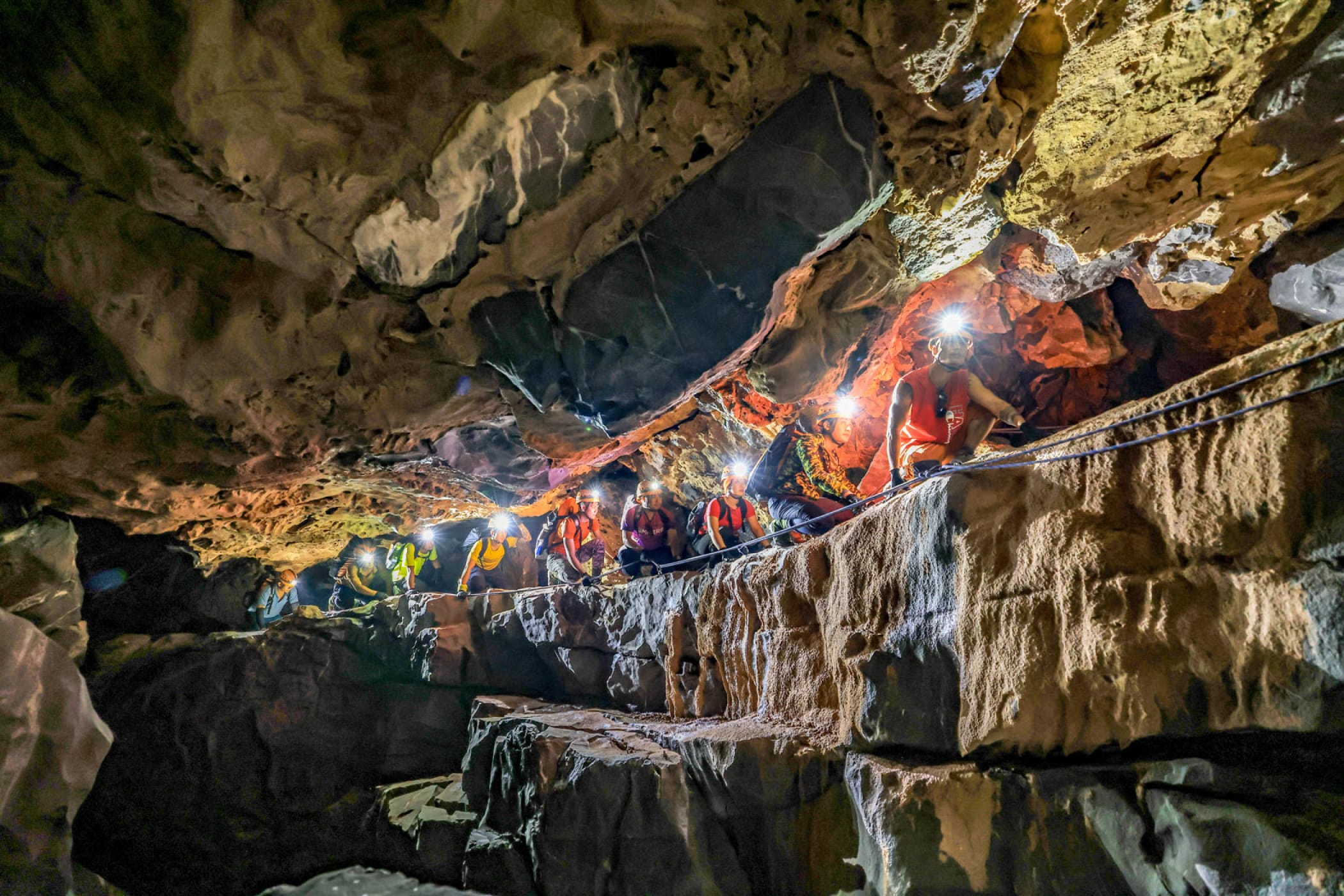 Expedition group walking single file through a river gorge below karst walls in Phong Nha