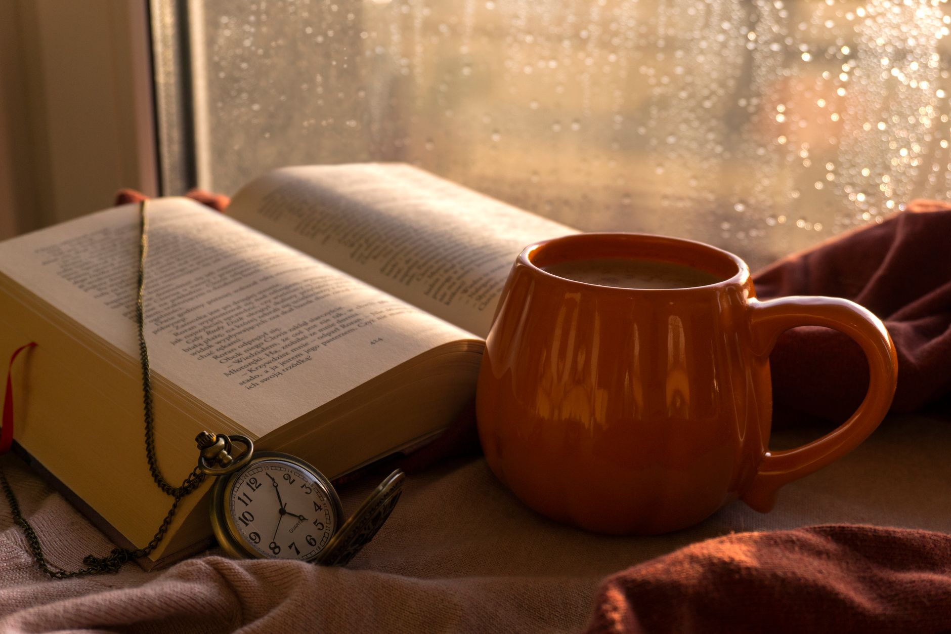 Rain running down a window above a coffee cup with green hills beyond