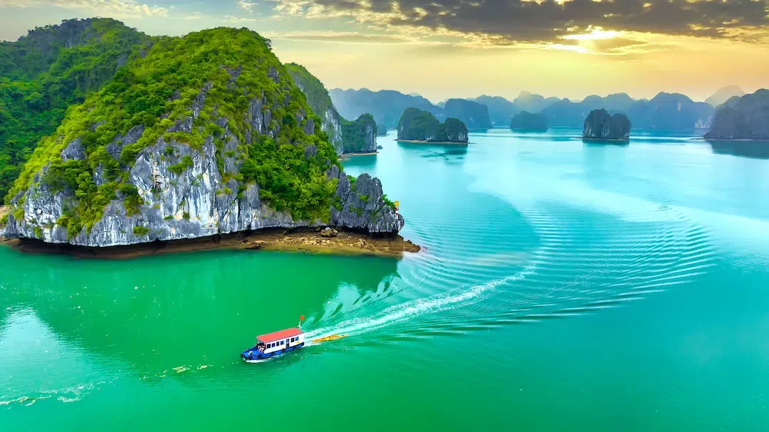 High angle view of a tourist cruise boat sailing past lush green karst mountains in Lan Ha Bay Vietnam.