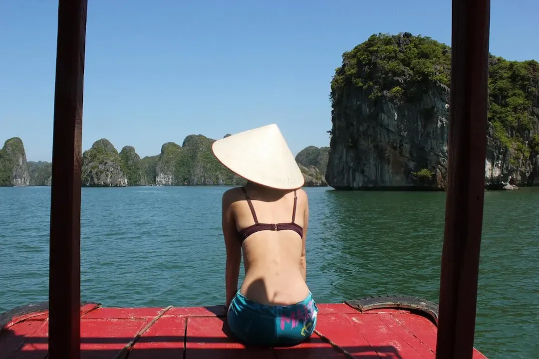 Woman in Conical Hat Sitting on Boat Deck Looking at Limestone Karsts in Lan Ha Bay Vietnam