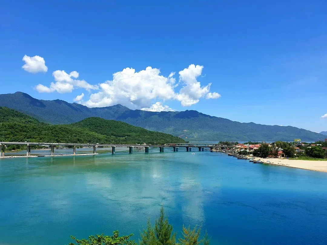 Lang Co Bay near Da Nang with iconic bridge spanning turquoise waters, lush green mountains, and sandy beach visible in a panoramic daytime view