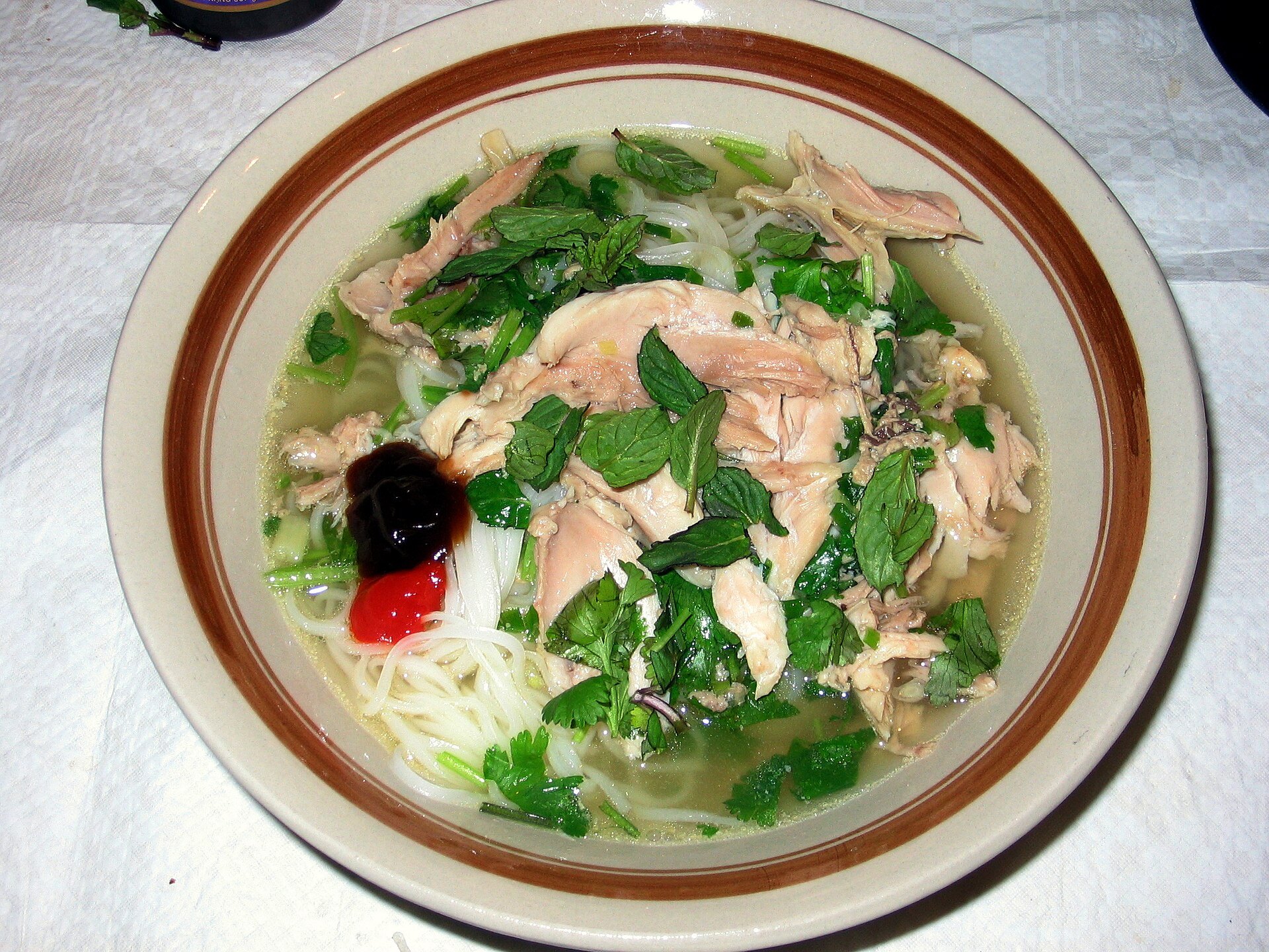 Chicken pho with flat rice noodles, fresh herbs and sauces in a bowl