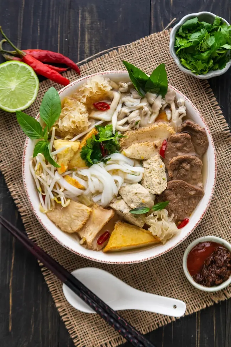 Bowl of pho chay with herbs, bean sprouts and lime on a metal table
