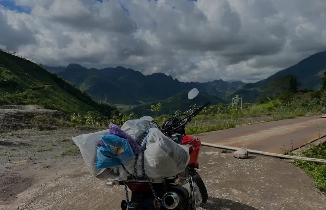 A loaded travel motorcycle parked on a mountain pass overlooking the dramatic green peaks of the Ha Giang Loop in Northern Vietnam.