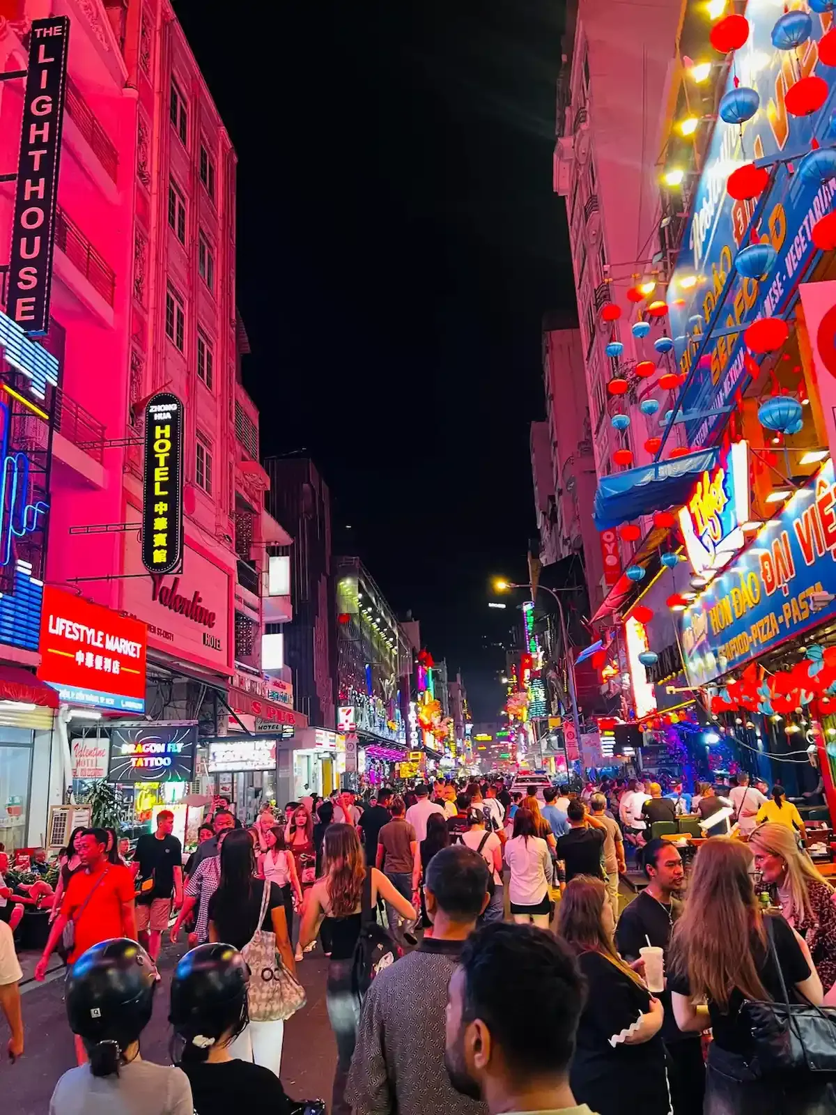 Bustling night scene at Bui Vien Walking Street in Saigon with neon lights, red lanterns, and crowds of tourists.