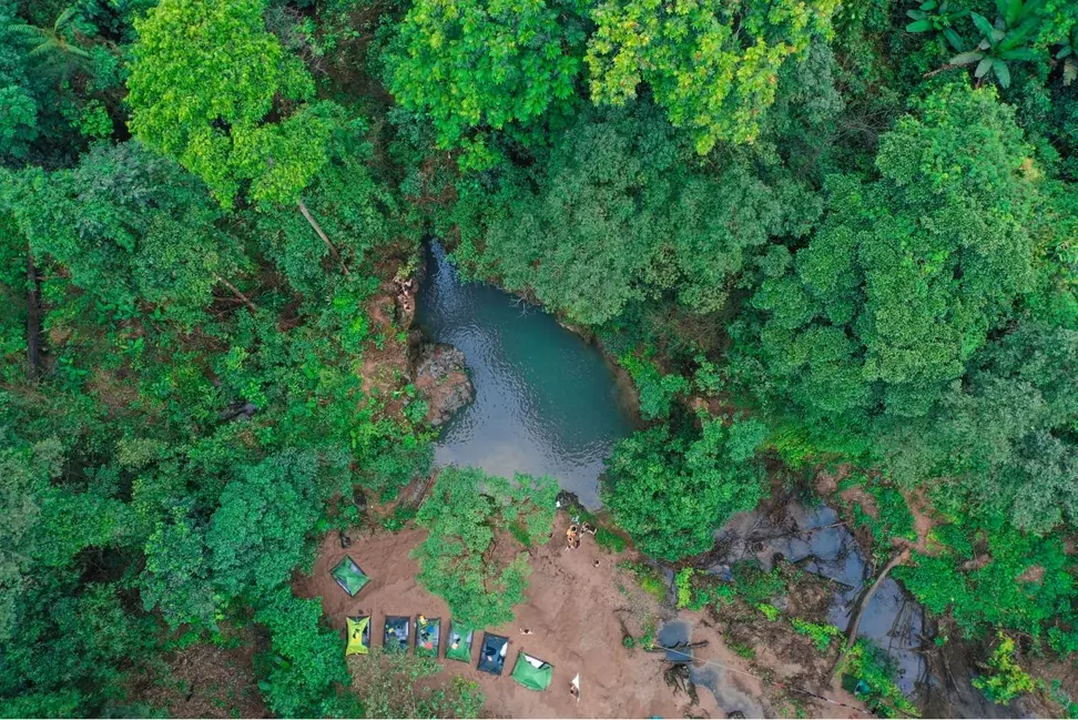 Aerial view of a jungle campsite with tents pitched beside a river pool