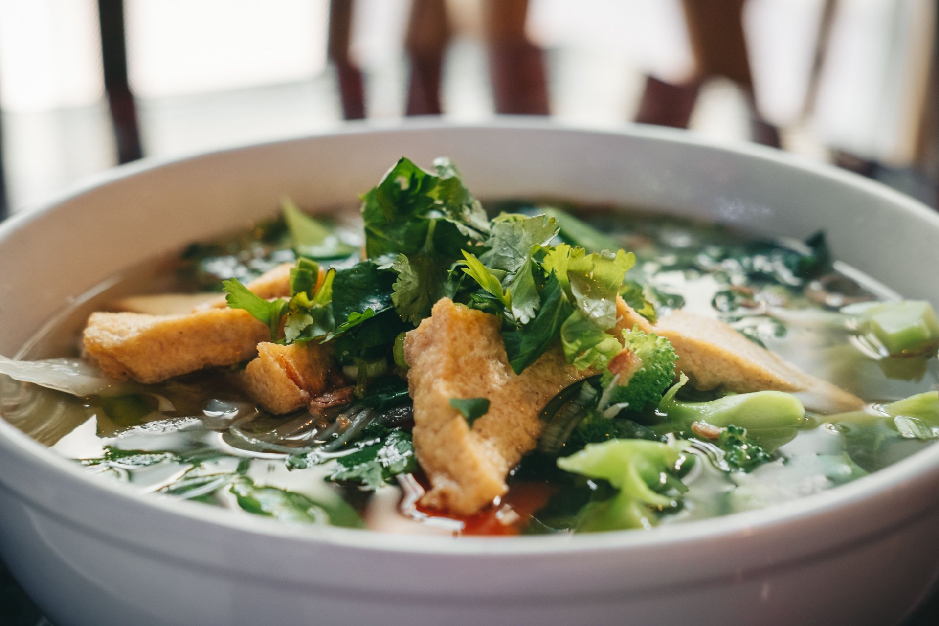 Golden tofu pieces and fresh green herbs topping a bowl of noodle soup