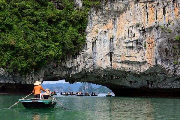 Scenic View of a Boat Entering Luon Cave, Surrounded by Green Cliffs.