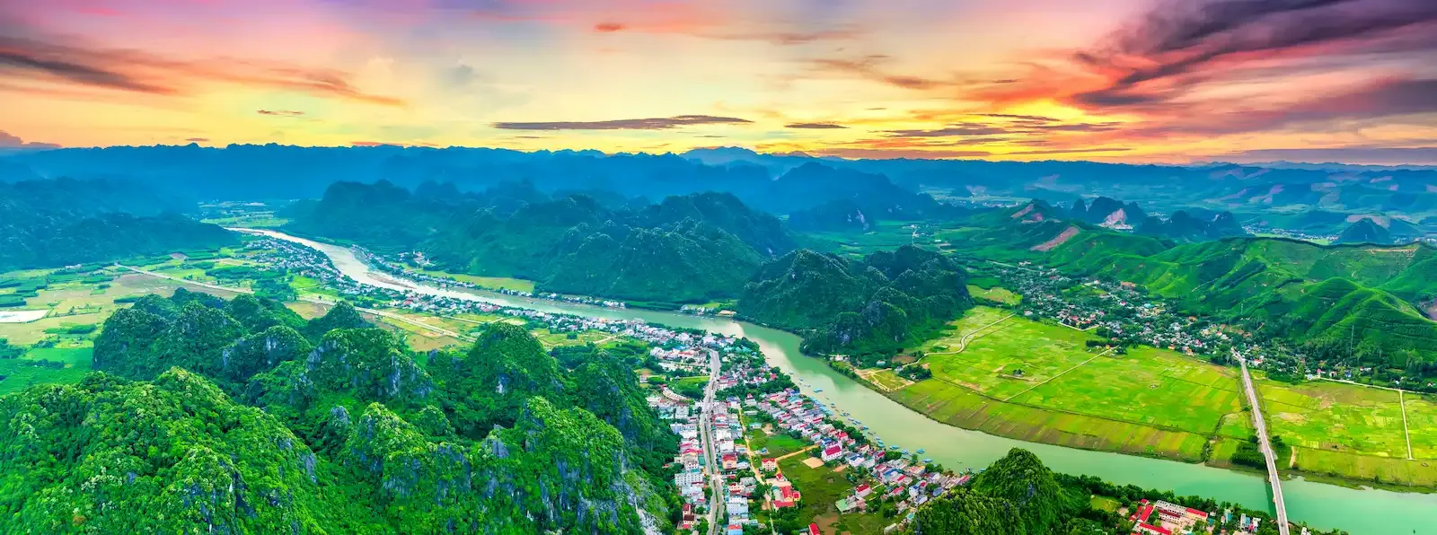 Panoramic aerial view of Phong Nha town and the Son River winding through karst mountains at sunset in Phong Nha Ke Bang National Park Vietnam, gateway to Son Doong Cave tours.