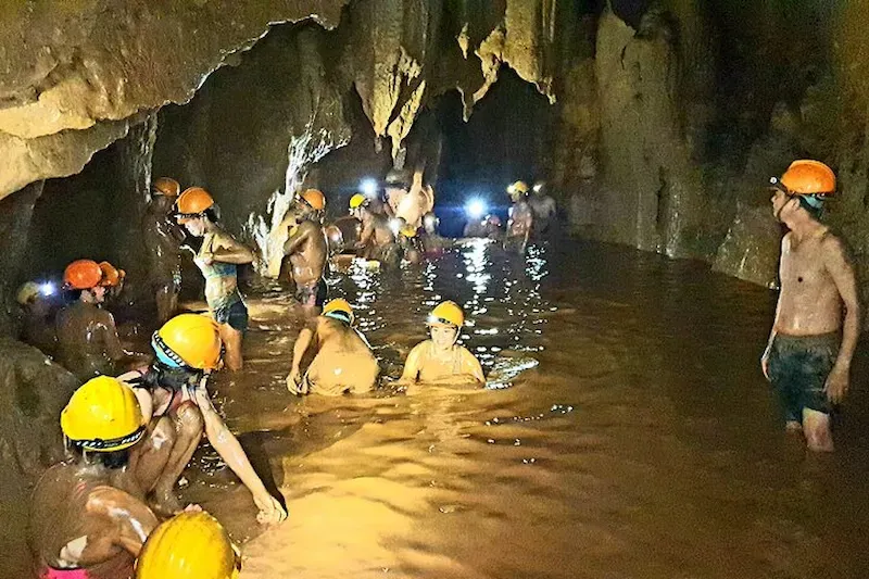 Dark Cave Interiors Shot of Vietnamese Tourists Enjoying Wading Through Muddy Waters in Phong Nha