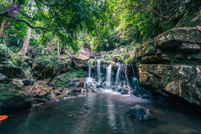 a Small Waterfall in Phong Nha Botanical Garden, Cascading Into a Tranquil Pool, Surrounded by Rocky Cliffs and Lush Green Forest