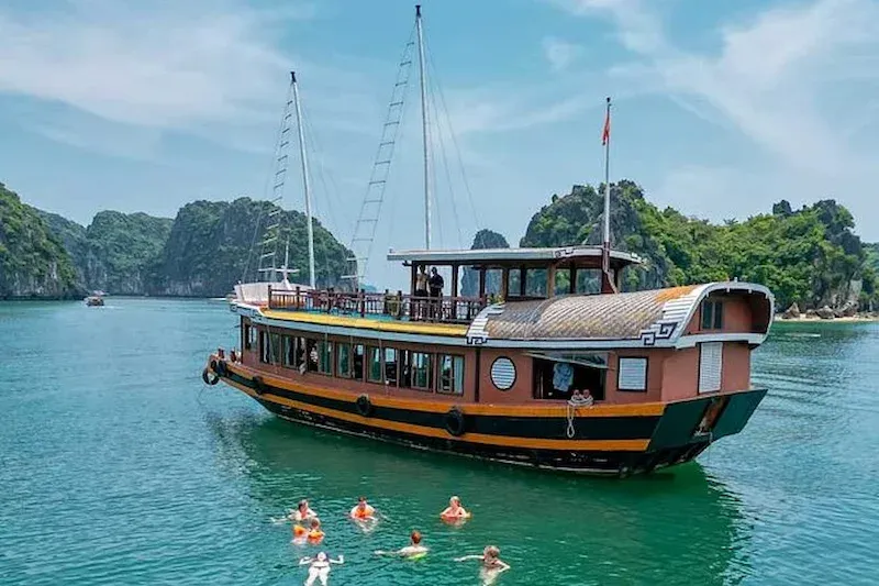 Traditional Wooden Tourist Boat in Lan Ha Bay With People Swimming in Emerald Green Water Near Cat Ba.