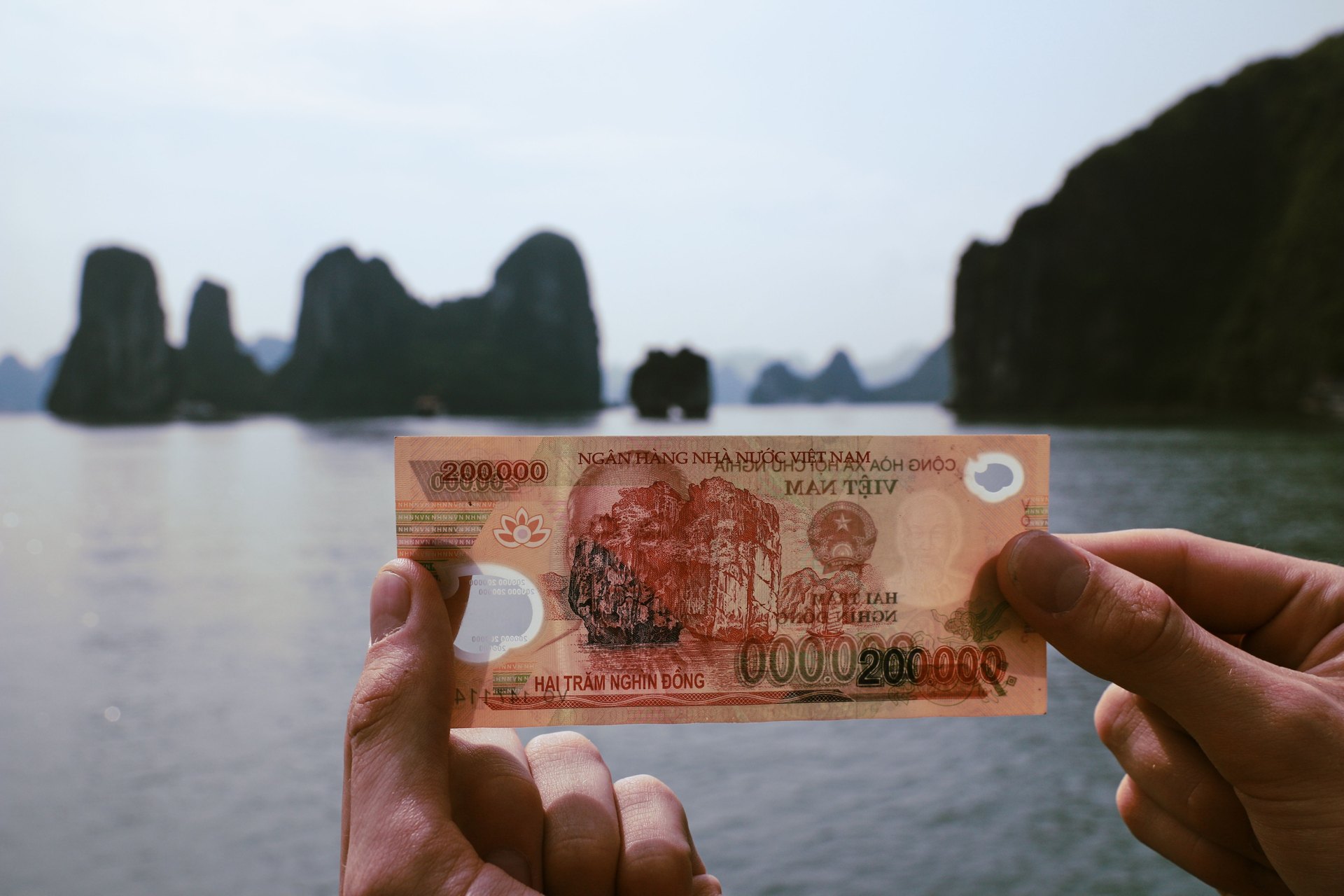 Hand holding a Vietnamese 200,000 dong note up against Halong Bay karsts