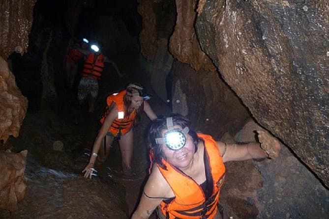 People Wearing Life Vests and Headlamps Crawl Through a Narrow, Rocky Cave Passage, Navigating the Wet and Rugged Terrain in Dark Cave, Phong Nha, Vietnam