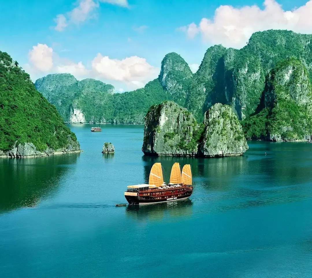 Traditional Junk Style Cruise Boat With Distinctive Red Sails Anchored in Emerald Green Waters of Bai Tu Long Bay Surrounded by Limestone Formations