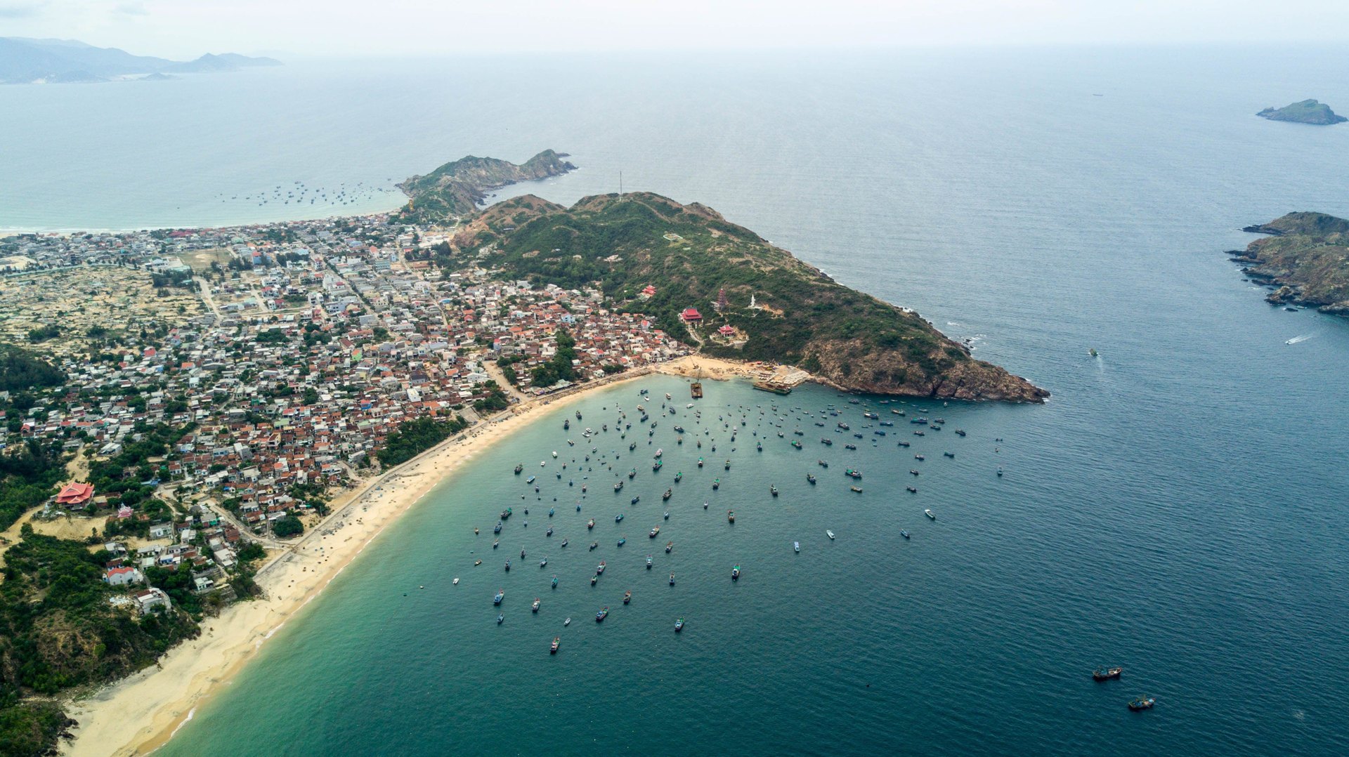 Aerial view of a fishing village on a headland with dozens of boats moored in the bay