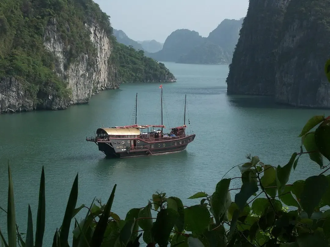 Traditional Red Wooden Junk Boat Anchored in Pristine Turquoise Waters of Bai Tu Long Bay With Limestone Islands and Pink Sunset Sky   Authentic Vietnamese Cruise Vessel