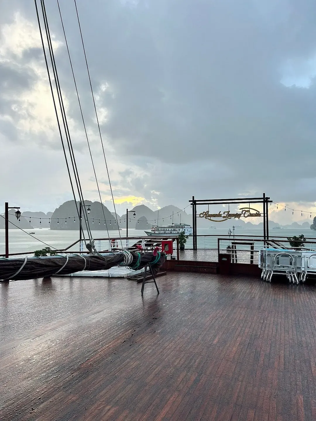 A Cruise Ship Deck With Lounge Chairs Overlooking Lan Ha Bay. the Image Captures the Deck Area on a Traditional Junk Boat With Views of Limestone Formations and Calm Bay Waters.