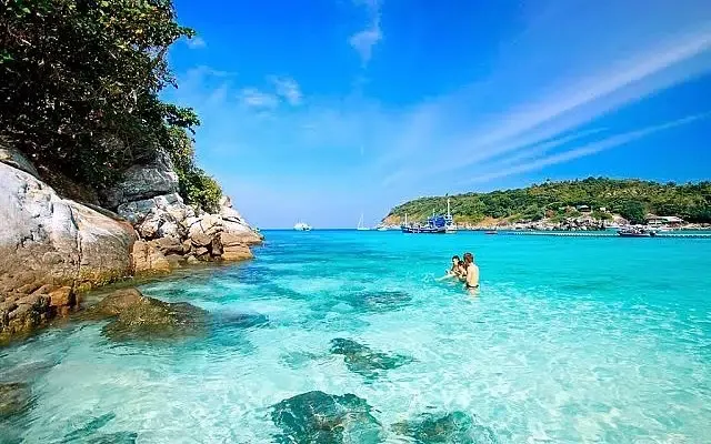 People swimming in crystal clear turquoise ocean water near rocky cliffs at Cham Island