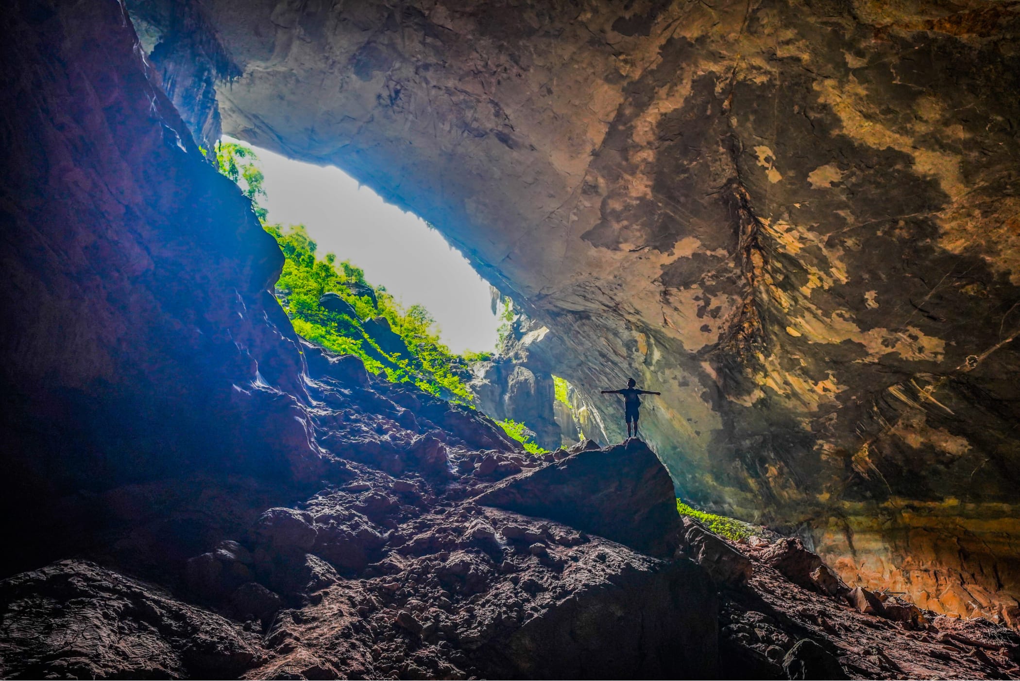 Caver silhouetted in a shaft of daylight entering a dark flooded cave passage