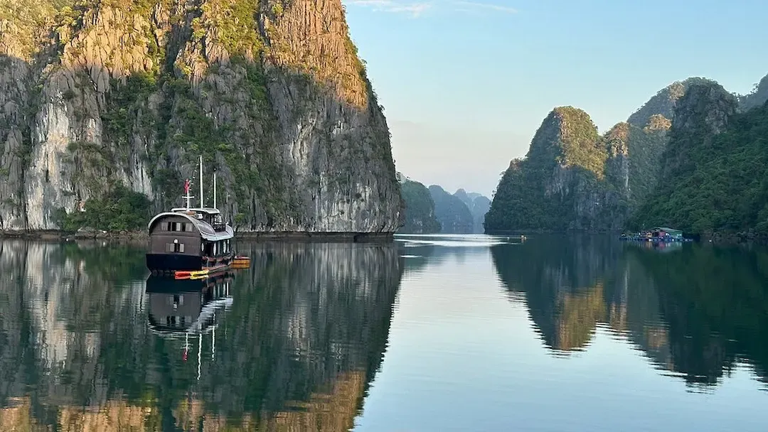 Lan Ha Bay Sunrise With Calm Emerald Water Traditional Boat and Limestone Cliffs Reflected on the Surface