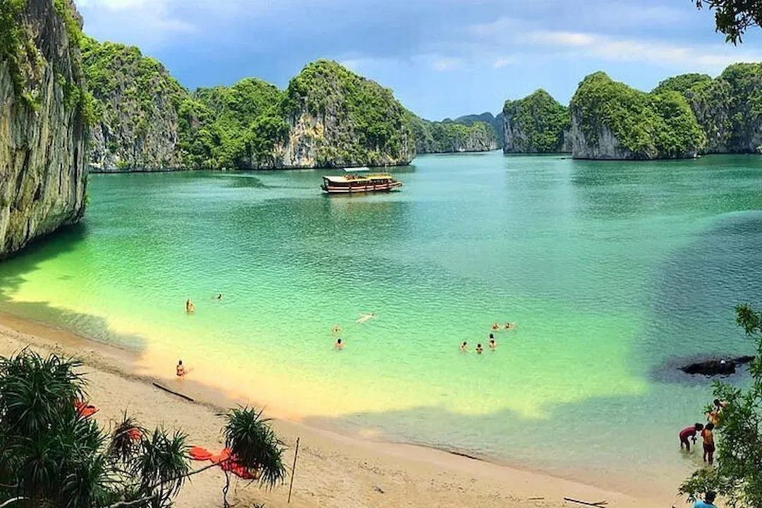 Beautiful Secluded Beach in Lan Ha Bay With Tourists Swimming in Crystal Clear Turquoise Water Near Limestone Cliffs.