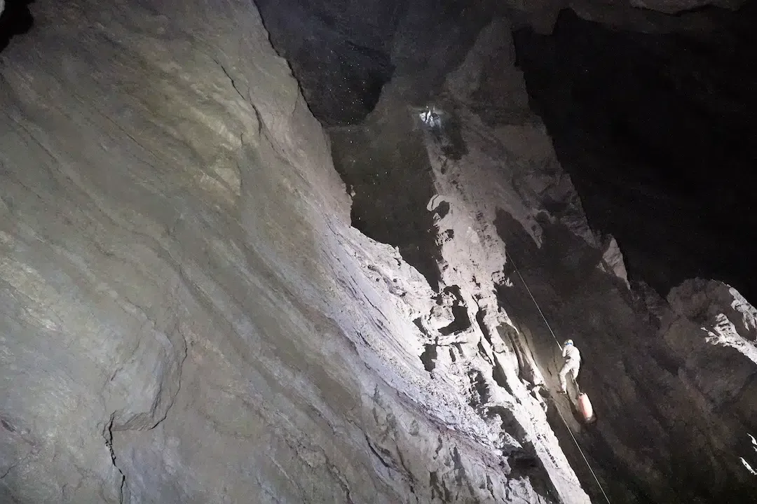 A lone explorer rappelling on a rope down a massive vertical shaft inside Veryovkina Cave, the deepest known cave on Earth.