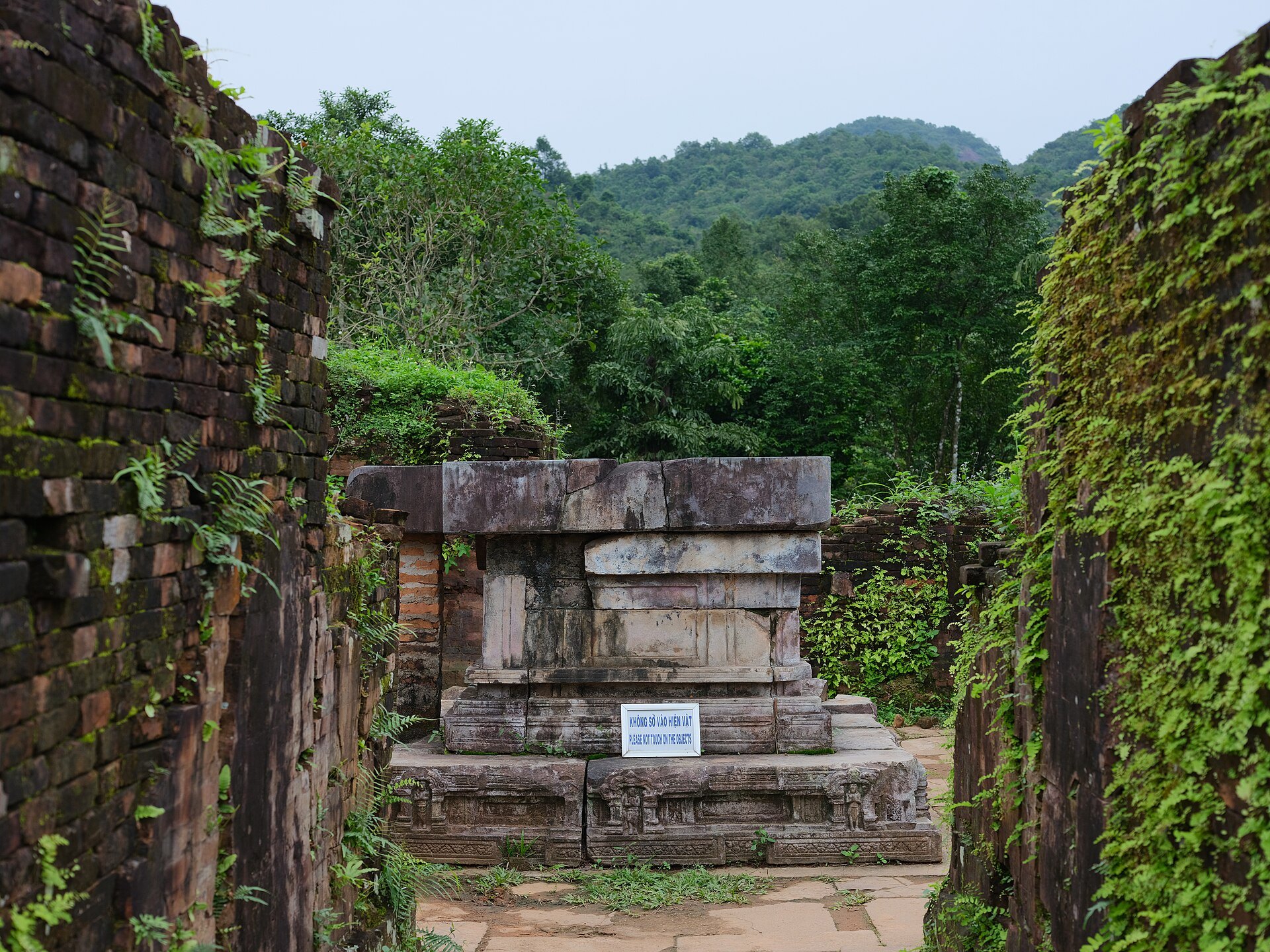 Stone yoni pedestal of temple A1 between ivy-covered brick walls at My Son
