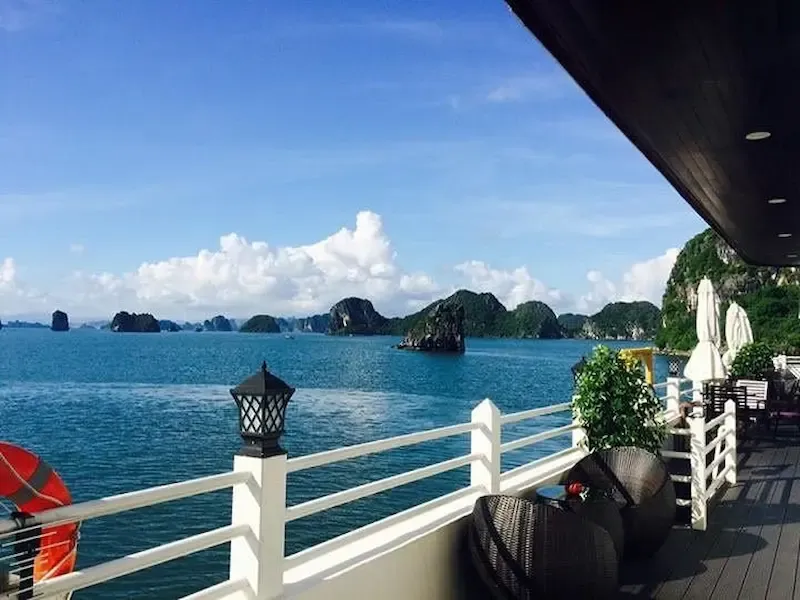 Luxury Cruise Ship Deck Overlooking Bai Tu Long Bay With White Railings, Clear Turquoise Water, and Dramatic Limestone Island Formations in Background