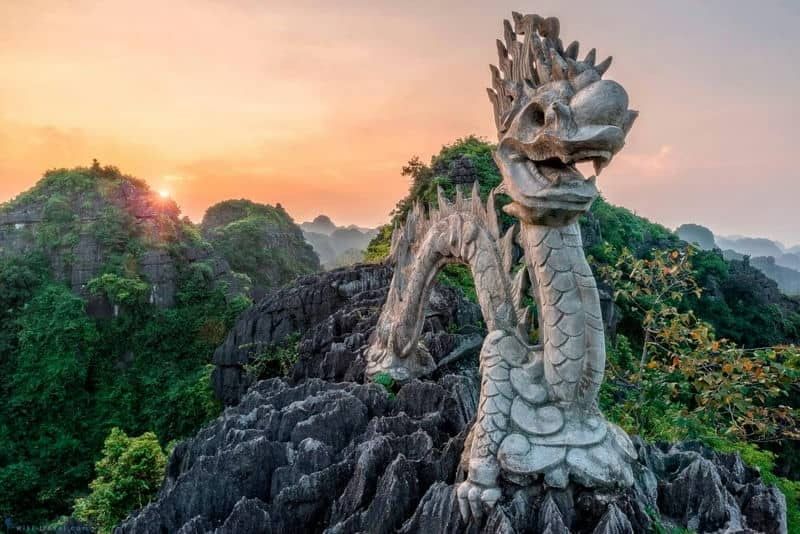 Stone Dragon Statue on Top of Mua Cave at Sunrise With Misty Mountains in the Background.