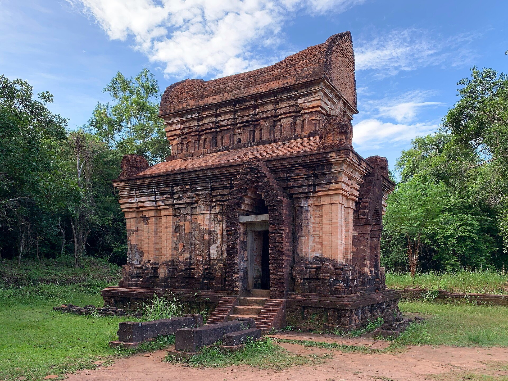 Small restored brick tower, Temple E7, standing on grass at My Son Sanctuary
