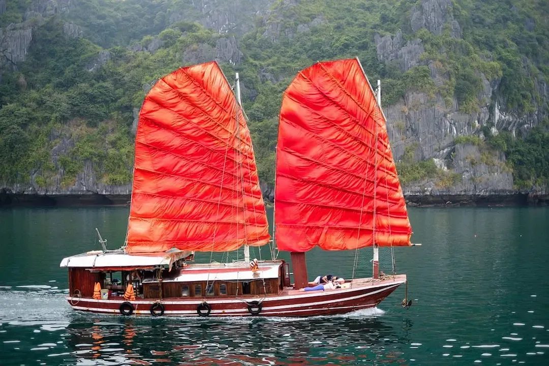 Traditional Indochine Style Junk Boat With Bright Red Sails Cruising on Emerald Waters of Lan Ha Bay