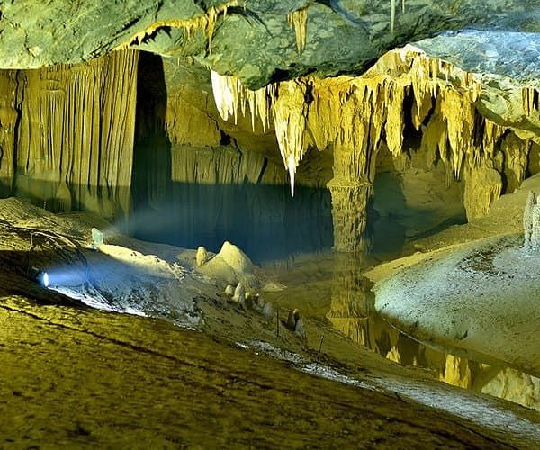 an Illuminated Underground Cave With Stalactites and Stalagmites Reflecting in a Calm Pool of Water, Creating a Serene and Mysterious Atmosphere