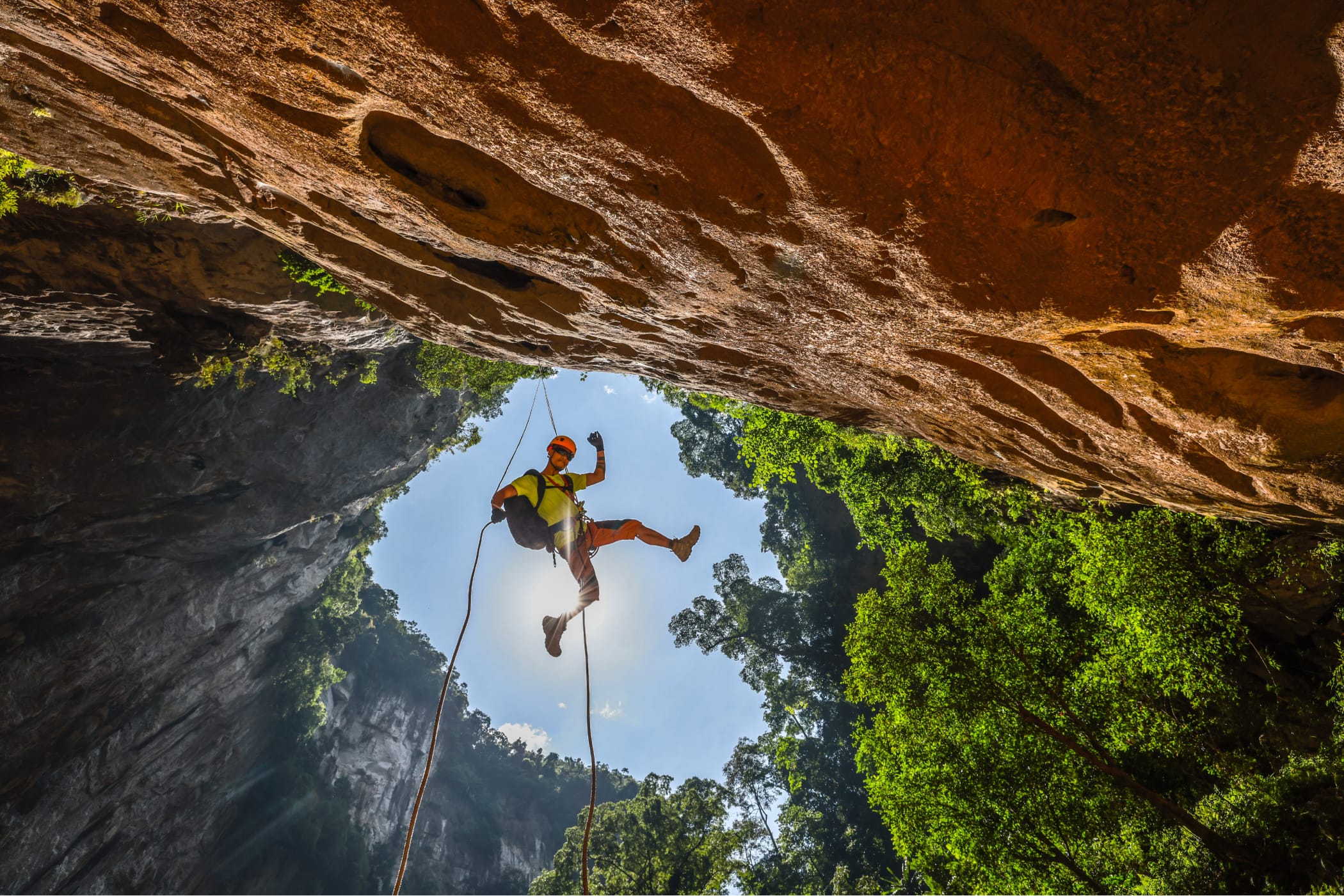Caver abseiling on a rope into a jungle doline, seen from below